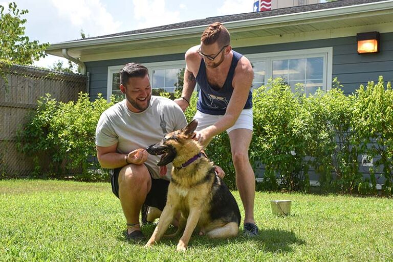 Two men with a dog in their front yard