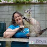 Danielle Bays wearing a blue shirt smiling at the camera. She has a cat next to her.