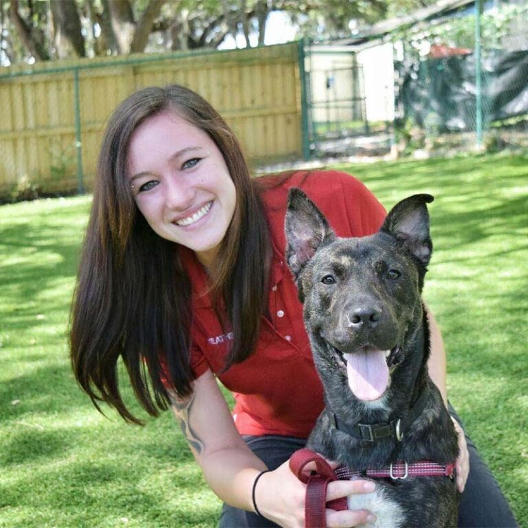 Heather wearing a red shirt, smiling at the camera with a black dog.