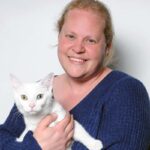 Joanna Fortin wearing a blue shirt and holding a white cat, smiling at the camera.