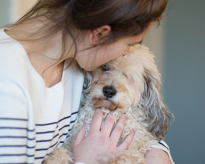 A woman holding her dog closely, kissing its face.