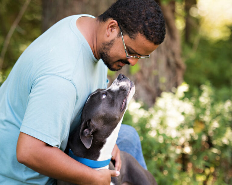 Black and white dog looking up at man wearing a blue shirt