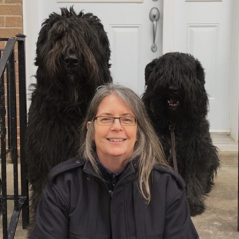 Kathy Duncan sitting on steps with two black fluffy dogs behind her.