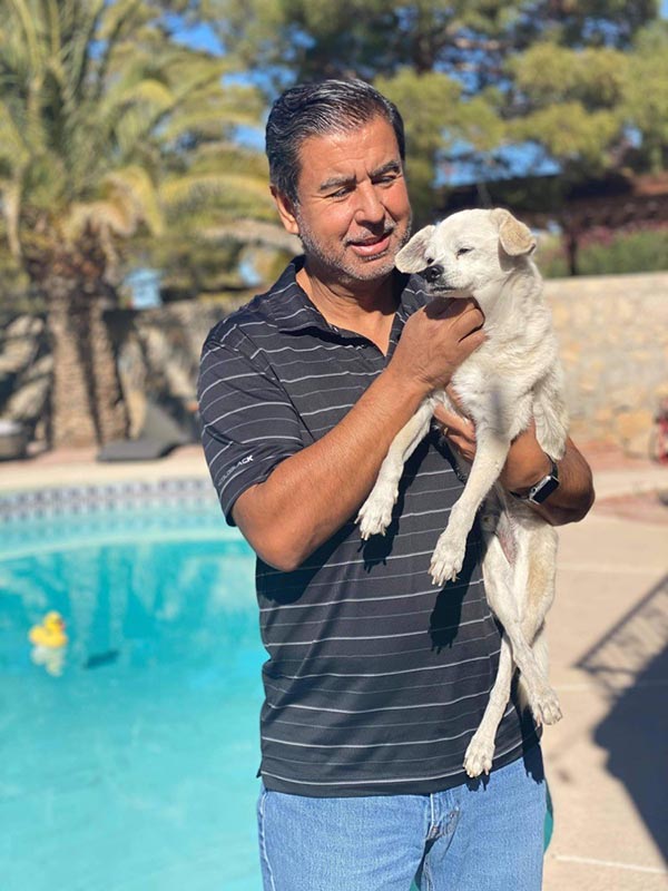 A man holding his small dog, Pancho, in front of a pool.