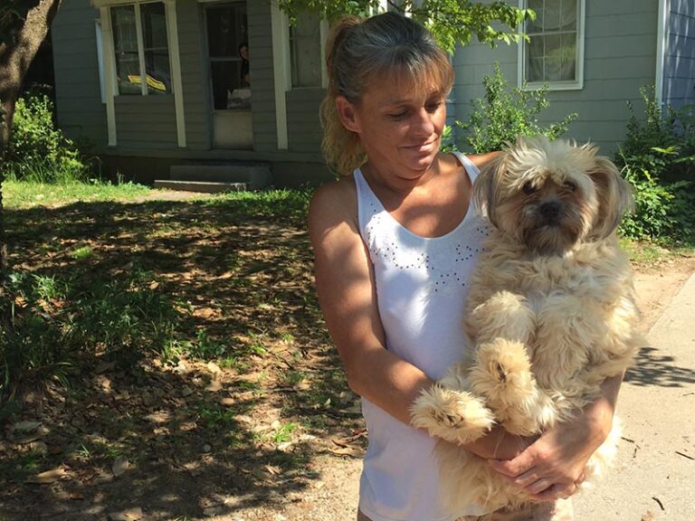 Woman holding her dog outside her house.